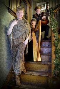 Diane Edgecomb in golden dress descending stairs with harper and guitarist on the stairs above.
